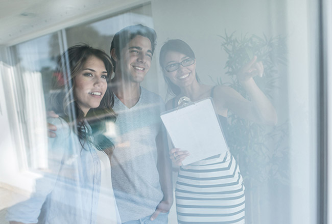 Couple with real estate agent looking outside window while real estate agent holds clipboard and points
