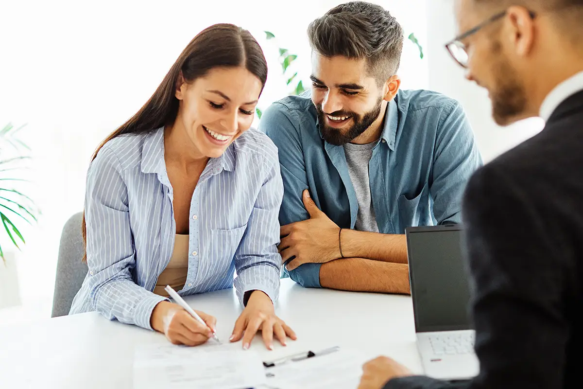 Two homebuyers signing paperwork with a real estate agent