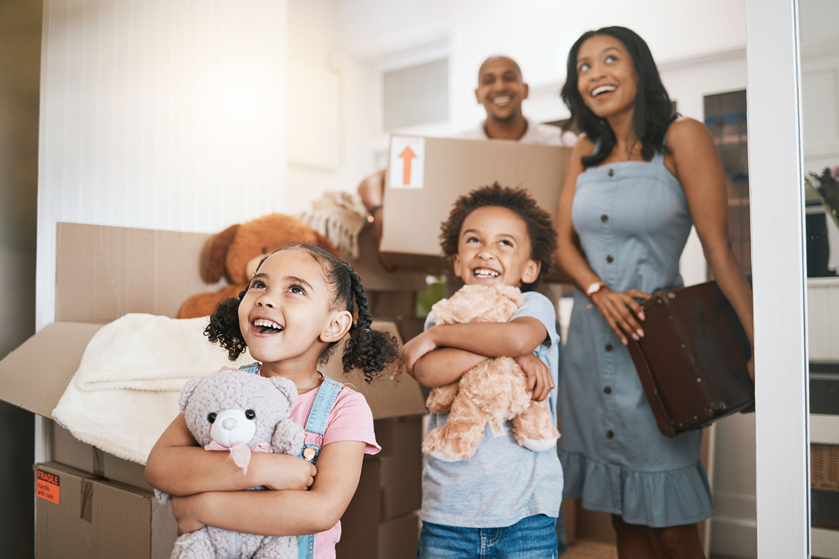 Parents and two children carrying moving boxes and items into a new home