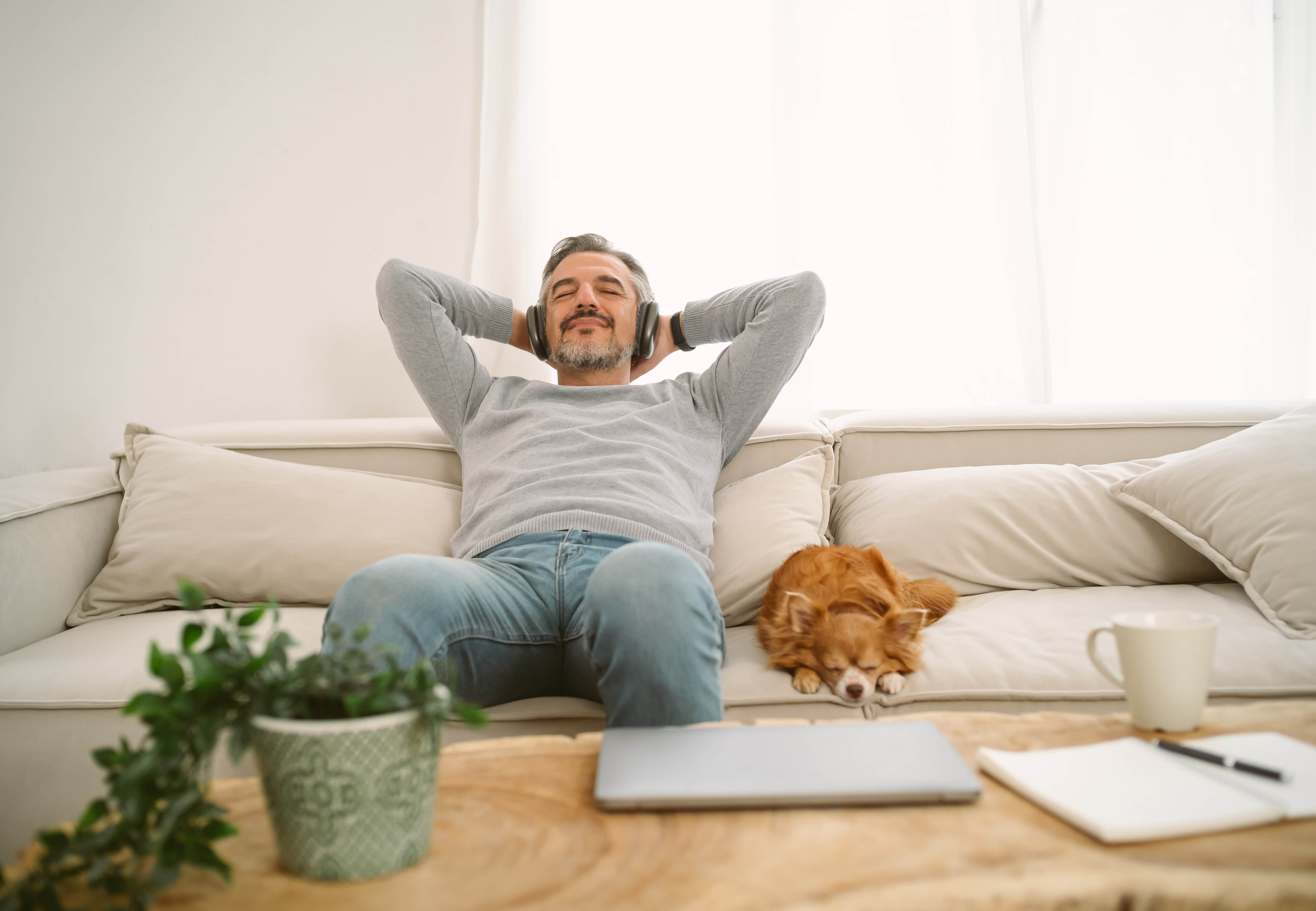 Man sitting on a couch next to his dog, listening to real estate podcasts on headphones