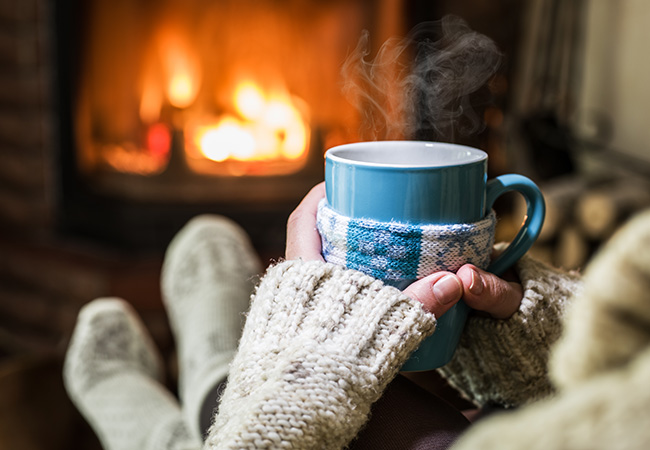 Someone holding a mug of hot cocoa while sitting in front of a fire