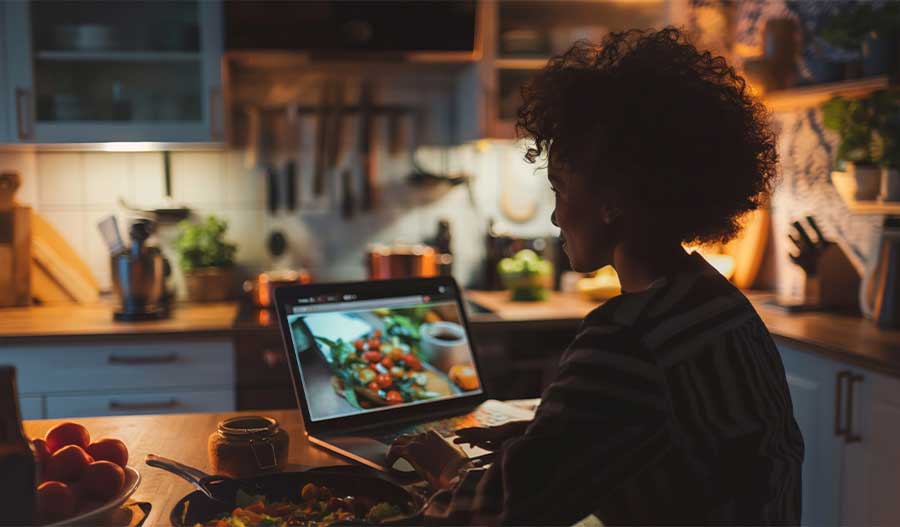 A woman sitting at a kitchen island, taking an online cooking class