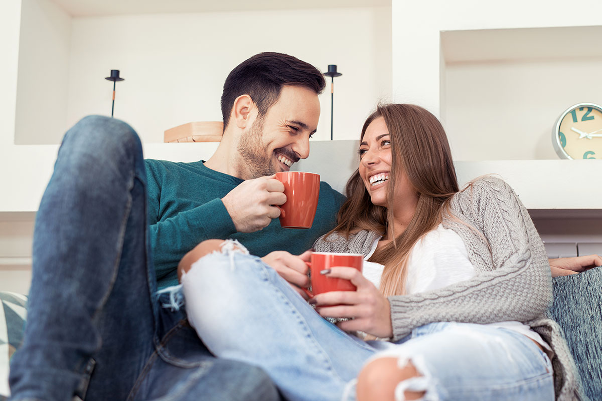 Couple drinking coffee and smiling on couch