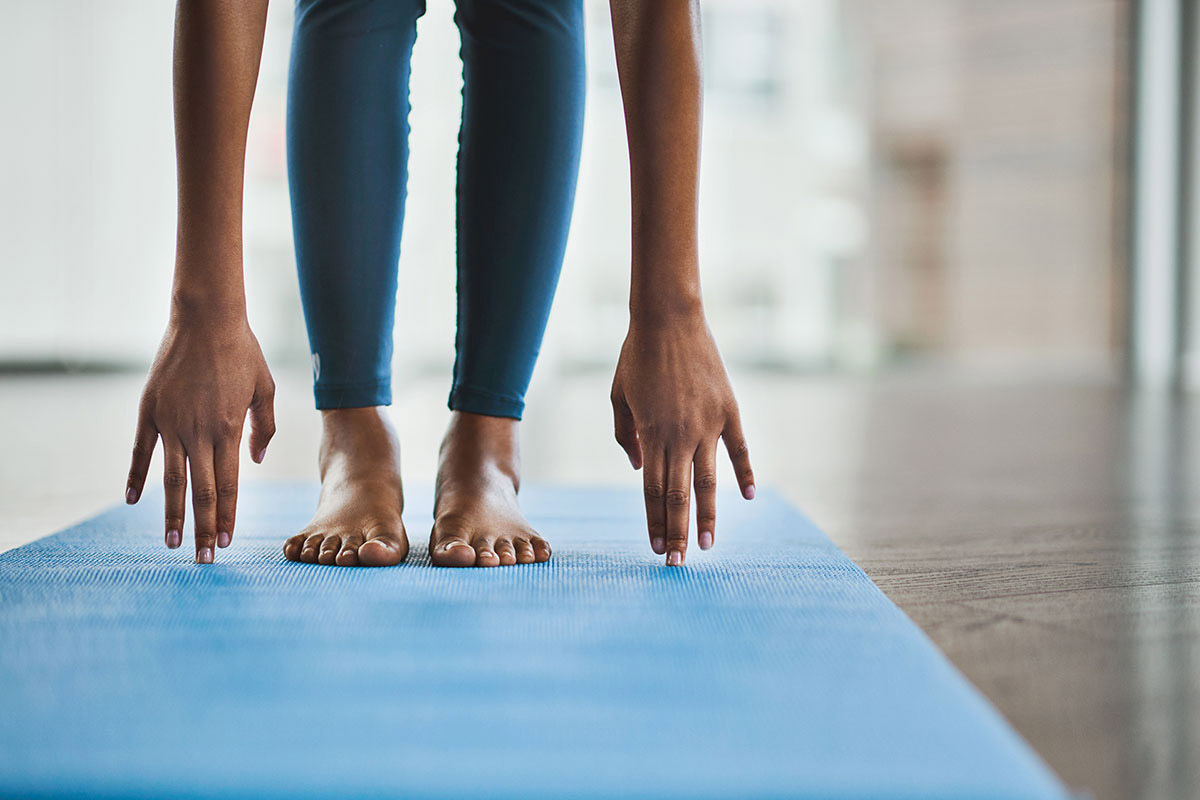 Feet on yoga mat with hands stretching to touch yoga mat