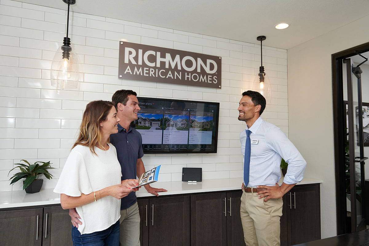 Couple holding brochure talking wtih sales associate in model home