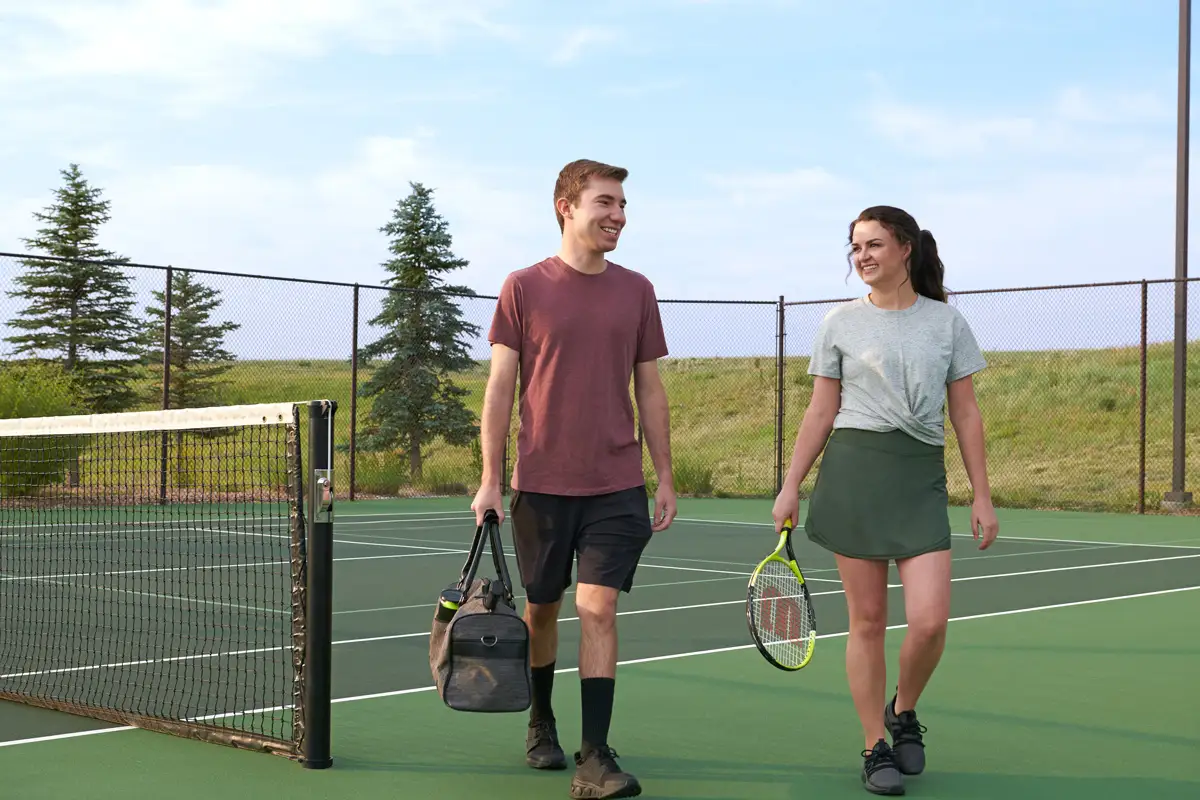Two people walking from tennis court smiling while holding bag and racket