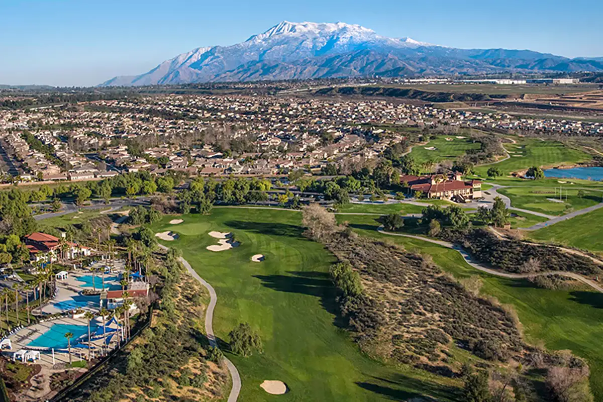 Aerial view of community with golf course, community center with pools, and mountains in the background