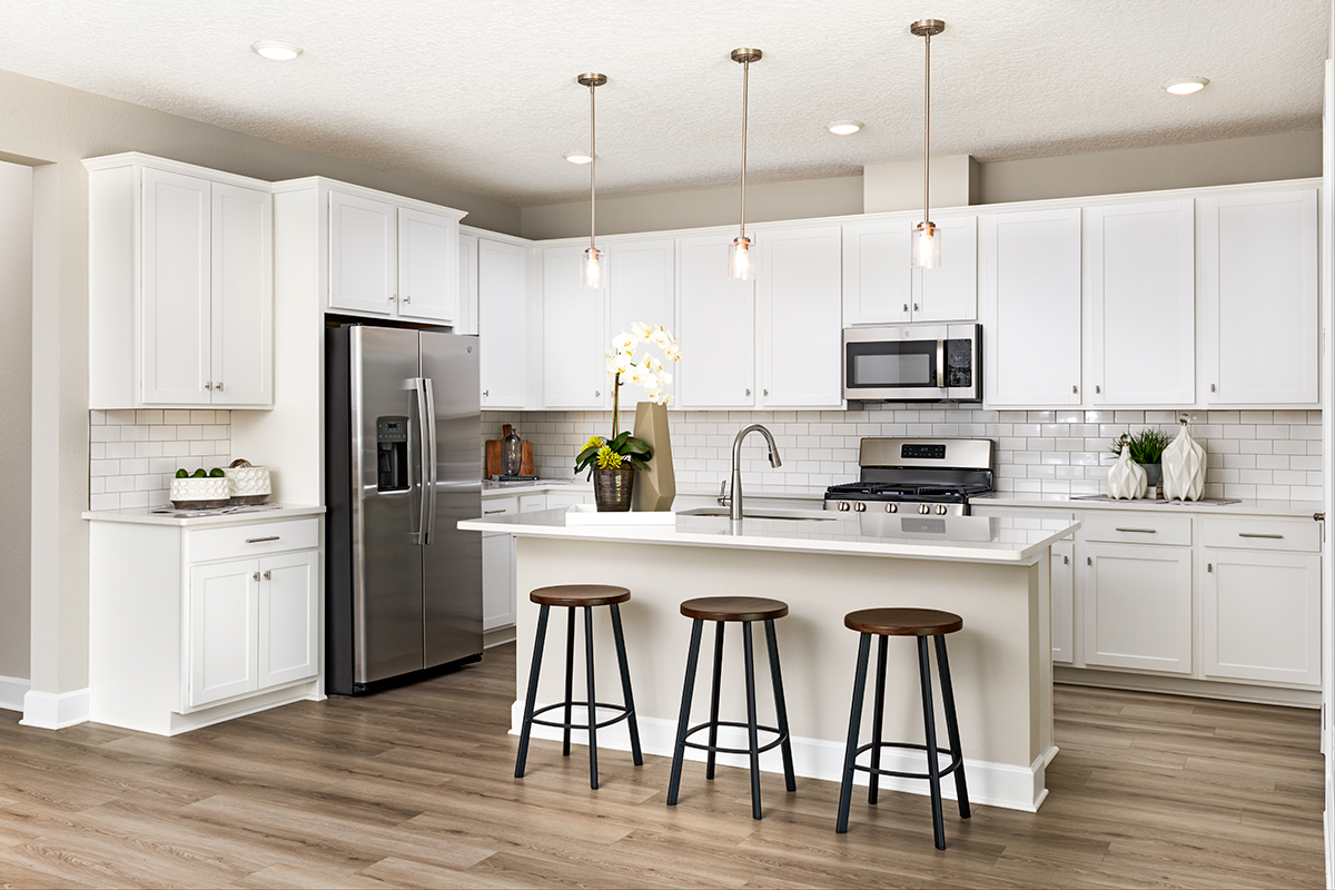 Kitchen with white cabinets and stainless steel hardware, with large white island and black stools